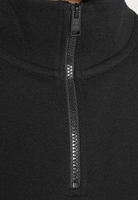 Primer plano de una cremallera de tela negra en una chaqueta de cuello alto, con el tirador de la cremallera mostrando el nombre de la marca "BOSS."