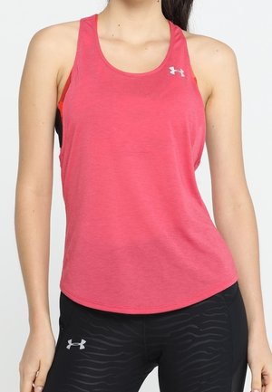 Femme portant un débardeur rouge de sport et un legging noir Under Armour avec un motif subtil, debout devant un fond blanc uni.