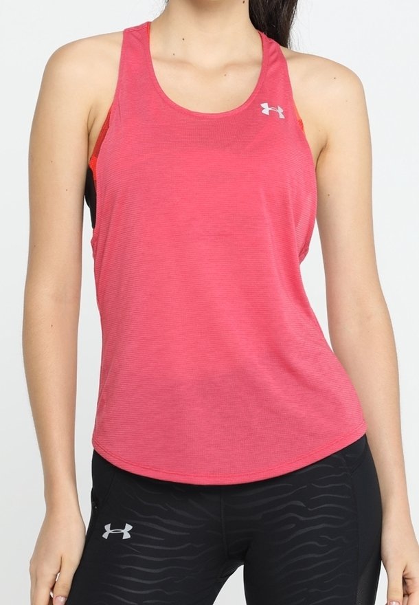 Femme portant un débardeur rouge de sport et un legging noir Under Armour avec un motif subtil, debout devant un fond blanc uni.