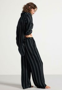 Set di abbigliamento casual a righe bianche e nere realizzato in tessuto morbido, con una maglietta dal taglio morbido con bottoni e pantaloni larghi con tasche.