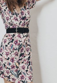 Vestido envolvente floral con mangas cortas, patrón de flores negras y pastel, cintura ceñida con un ancho cinturón negro, tejido ligero, hasta la rodilla.