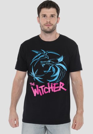 Schwarzes T-Shirt mit blauem Grafikdesign, das einen Wolf zeigt, und dem Text "THE WITCHER" in Pink. Kurzärmlig, Rundhalsausschnitt, aus Baumwollmaterial.
