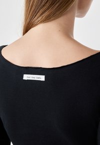 Indumento nero con un ampio scollo e una texture morbida. Un'etichetta sulla parte posteriore riporta la scritta "Cool Cosy Comfy". Le cuciture sono a taglio vivo.
