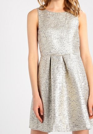 Sleeveless silver metallic textured dress with fitted bodice and pleated skirt worn by a person with loose hair.