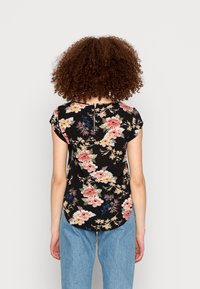 Top floral com fundo preto, mangas curtas, bainha arredondada e fenda na gola costas. Padrões florais vibrantes em rosa, amarelo e azul.