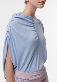 Lichtblauw, gathered top met zijdraping, met een zachte textuur en korte mouwen, gecombineerd met een geplisseerde lila rok.