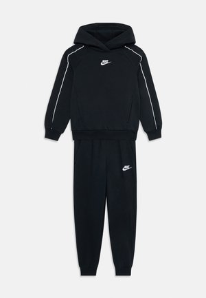 Ensemble hoodie et joggers noir Nike avec des piping blancs sur les manches et des logos sur la poitrine et la cuisse gauche.