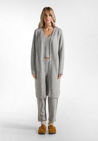 Grau gestrickte Strickjacke über einem grauen Cropped-Top und passenden Hosen. Das Outfit hat einen lockeren Schnitt, eine weiche Textur und gesenkte Schulterähte.