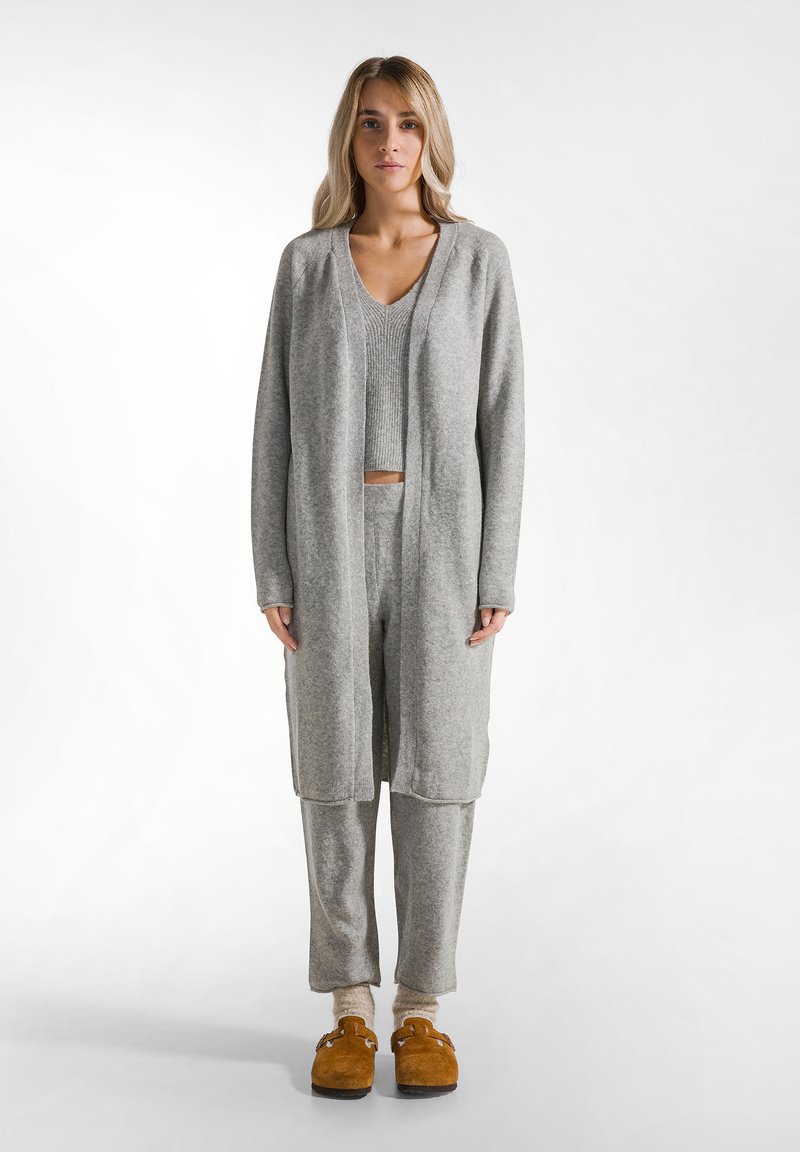 Grau gestrickte Strickjacke über einem grauen Cropped-Top und passenden Hosen. Das Outfit hat einen lockeren Schnitt, eine weiche Textur und gesenkte Schulterähte.