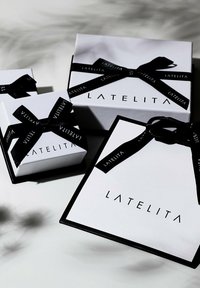 Tre vita presentaskar med svarta accenter och band, med varumärket "LATELITA" i fet stil på varje låda.