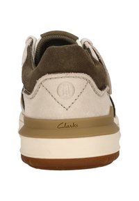 Braune Wildleder- und beige Leder-Schuhe mit einem abgerundeten Design, ausgestattet mit einer Gummisohle und einem geprägten Logo an der Ferse.
