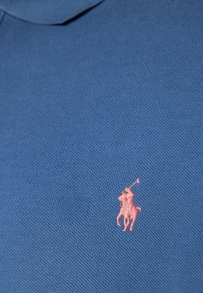 Zila polo krekls ar teksturētu audumu. Izcelšanās ir neliels rozā izšūts logo ar jātnieku kreisajā krūšu daļā.