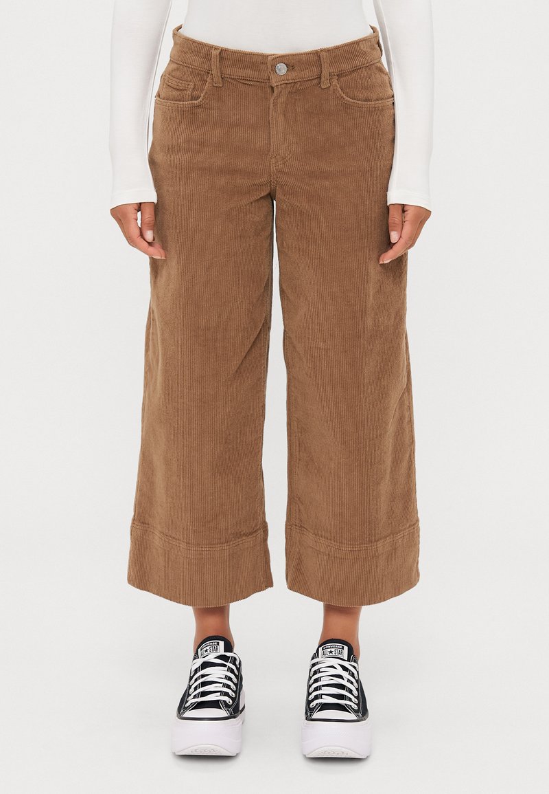 Bruine corduroy wijde broek met een hoge taille, voorzakken en omgeslagen hems, gecombineerd met zwart-witte sneakers.