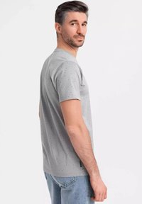 Camiseta gris de manga corta con un patrón moteado, cuello redondo y un detalle de abertura en el costado, combinada con jeans de color azul claro.