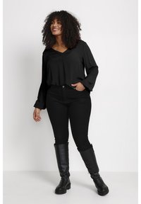 Blouse noire avec un décolleté en V et de longues manches évasées, accompagnée de jeans noirs ajustés et de bottes en cuir noires jusqu'aux genoux. Texture lisse tout au long.