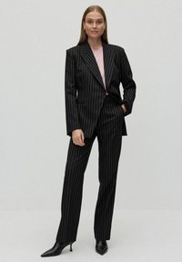 Svart randig kostym med skräddarsydd kavaj och raka byxor, i kombination med en ljusrosa topp. Har skarpa slag och en elegant silhuett.