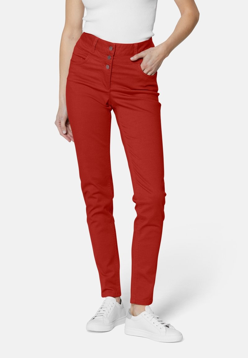 Pantalones ajustados rojos con cintura alta, cierre de tres botones y bolsillos frontales. Combinados con zapatillas blancas para un contraste. Textura de tela suave.