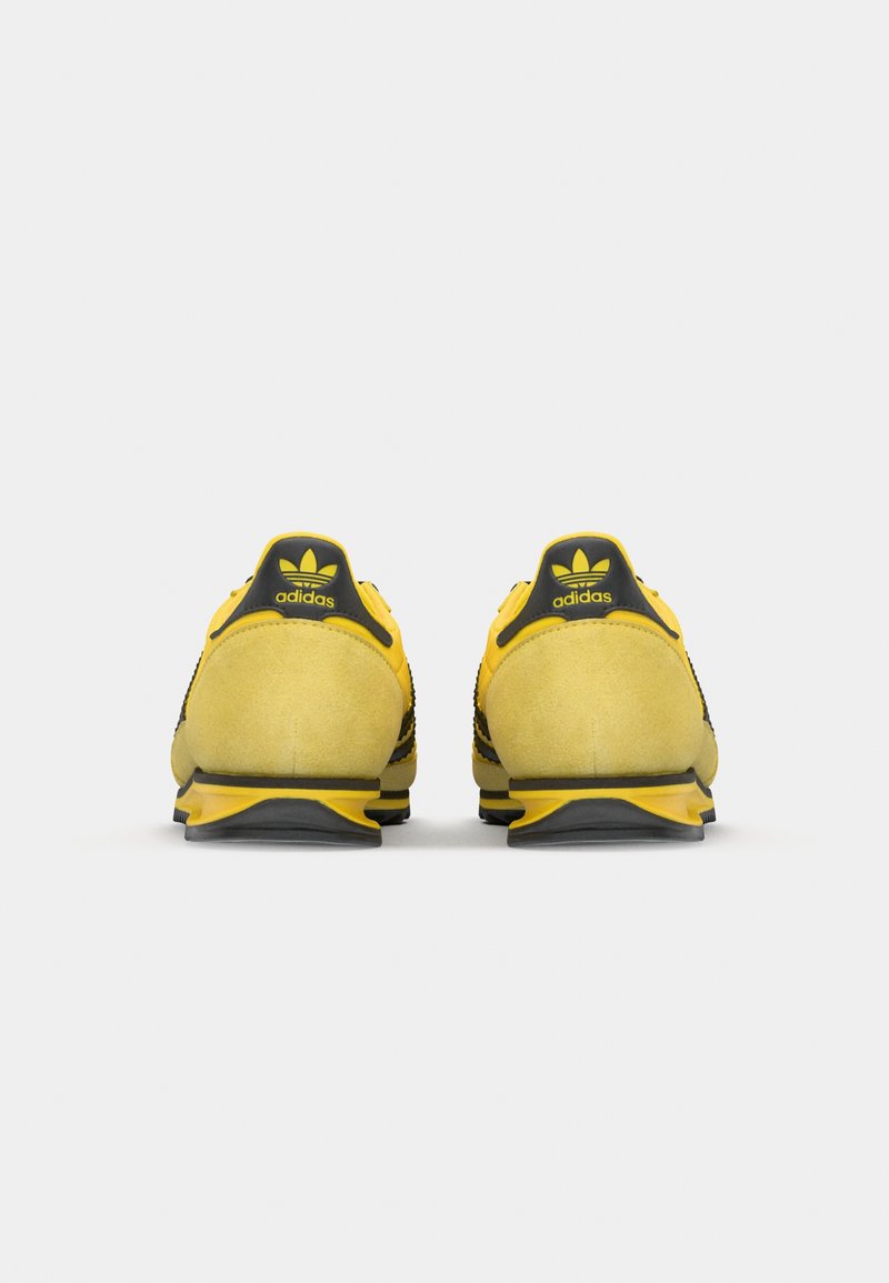 Zapatillas Adidas con un upper de ante amarillo, acentos de malla negra y una suela de goma. Presenta una marca negra y verde en el talón.