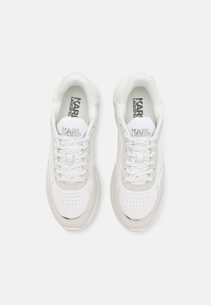 Zapatilla blanca con paneles de cuero liso y gamuza, caja de dedo perforada y cordones planos. Texto del logo en la lengua y la plantilla. Suela redondeada.