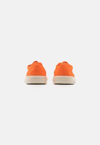 Orange canvas sneakers med låg profil, beige gummisulor och enkla sömmar på baksidan och sidorna.