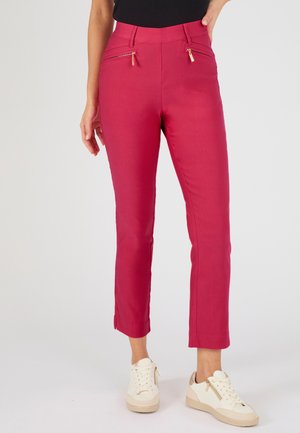 Mujer con pantalones rosas ajustados y cortos con bolsillos delanteros con cremallera y zapatillas blancas con suelas beige y cremalleras.