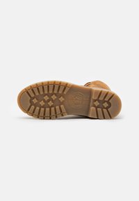Sola de botas de couro castanho com um fundo de borracha texturizada apresentando padrões circulares e geométricos, logo em relevo e detalhes de reforço.
