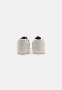 Adidași din piele albă cu spate rotund, călcâi texturat și talpă din cauciuc. Prezintă un design minimalist și un mic logo al mărcii pe călcâi.