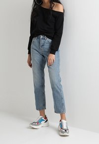 Sudadera negra de un solo hombro, jeans de tiro alto en azul claro y zapatillas multicolores con acentos en rojo, azul y gris. Estilo casual.