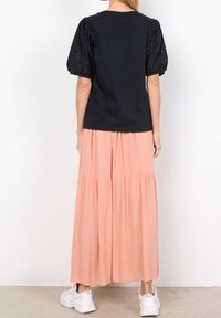 Czarny top z bufkami z koronki; w połączeniu z wielowarstwową, brzoskwiniową spódnicą maxi. Dopełnieniem stroju są białe trampki.