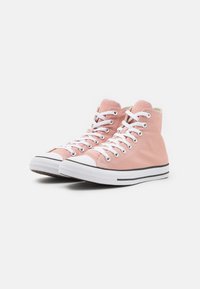 Zapatillas altas de lona rosa con cordones blancos, puntera de goma y suela blanca con rayas negras.