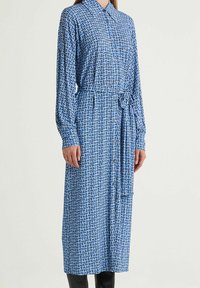 Abito camicia con motivo blu, collo a camicia, maniche lunghe, chiusura con bottoni, cintura in vita e design geometrico in varie tonalità di blu.