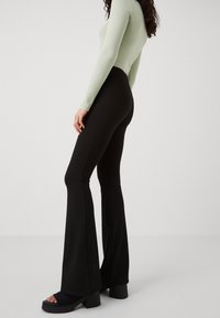 Svarta utsvängda byxor i ett elastiskt tyg, ihop med en ljusgrön ribbad långärmad topp. Har en åtsittande midja och design med utsvängda ben.