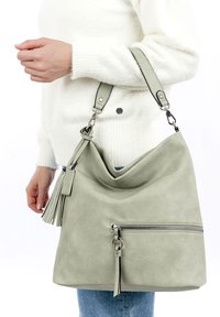Bolso de hombro de imitación cuero gris con un diseño relajado, superficie texturizada, bolsillo frontal con cremallera y acento de borlas en la correa.
