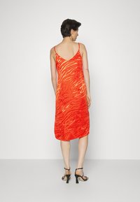 Vestido slip vermelho com padrão de riscas de tigre, feito de tecido leve. Alças finas e corte a meio comprimento, com um acabamento ligeiramente texturizado.