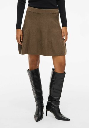 Jupe en tricot marron avec une silhouette évasée et une taille côtelée, associée à de grandes bottes en cuir noires avec des pointes et des talons aiguilles.