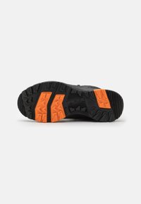Talpa de pantof sport negru cu crampoane adânci, având accente vibrante de portocaliu și o suprafață texturată pentru aderență și stabilitate.