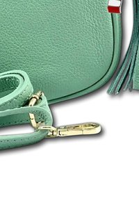 Mintgroene leren handtas met een textuur oppervlakte, een afneembare schouderriem en gouden hardwareaccenten; heeft een kwastje aan de zijkant.