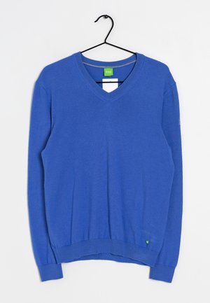 Maglione blu a scollo a V realizzato in tessuto morbido, con maniche lunghe, polsini e orlo a costine, dotato di un piccolo etichetta verde sul lato sinistro in basso.