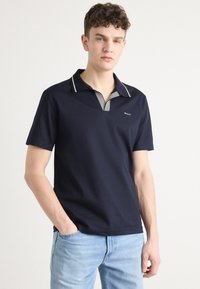Polo de color navy con mangas cortas, cuello a rayas y logotipo en el pecho. La camiseta tiene una textura suave y un corte clásico.