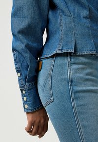 Dongerijakke med knapper ved ermene i mørkeblå, sammen med lyseblå jeans med et logopatch og distinkt lommebroderi.
