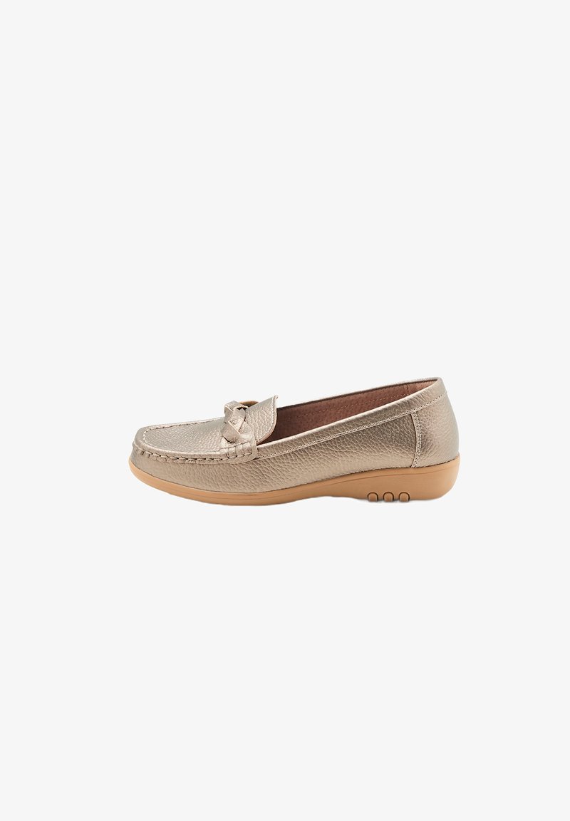 Mocasin metálico dorado con parte superior de cuero texturizado, un lazo decorativo en la parte frontal y una suela de caucho color beige con tres detalles circulares de agarre.