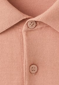 Gros plan sur un polo en tricot rose clair montrant le col et deux boutons assortis fermés sur la patte de boutonnage avant.