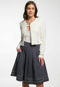 Weiß gestrickte, kurze Jacke mit rundem Ausschnitt und silbernem Zubehör, kombiniert mit einem dunklen, ausgestellten Rock aus strukturierter Stoff und dekorativem Besatz.