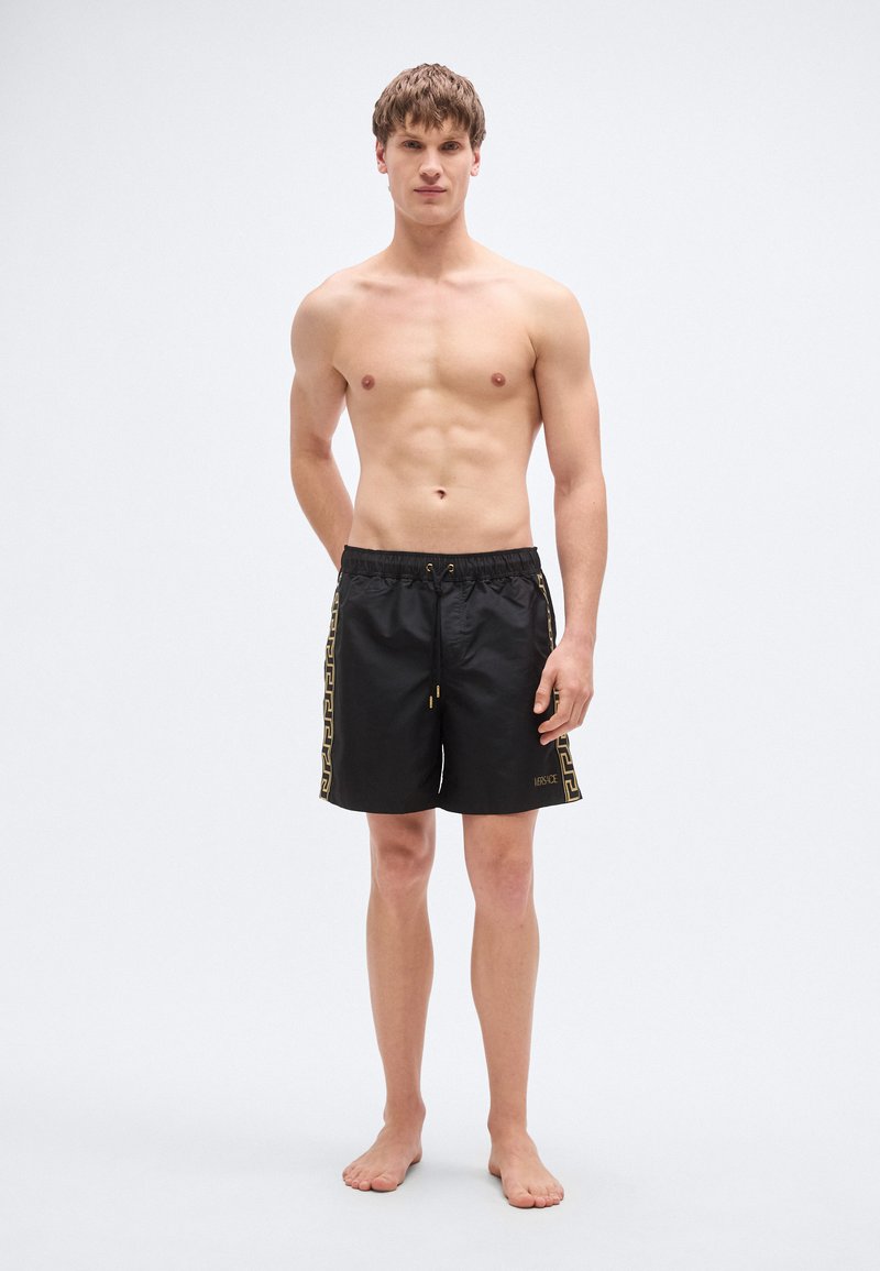 Shorts de bain noirs avec une taille à cordon, arborant un motif grec doré le long des côtés et un tissu lisse et léger.