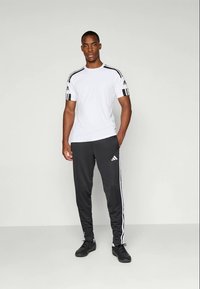 Hvit athletic t-skjorte med svarte striper på skuldrene, kombinert med svarte joggebukser med hvite sidestiper og logo.