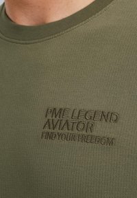 Camiseta de algodón verde oliva con cuello redondo acanalado, que presenta un texto en relieve con la marca "PME LEGEND AVIATOR FIND YOUR FREEDOM" en la parte delantera.