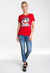 Red cotton t-shirt featuring a graphic of a superhero and text "Girls Will Save the World," paired with blue skinny jeans and black platform sandals.