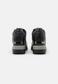 Pár černých platformových tenisek s hustými šedými a černými podrážkami, lesklými akcenty a texturovanými bočními panely zobrazenými ze zadní strany.