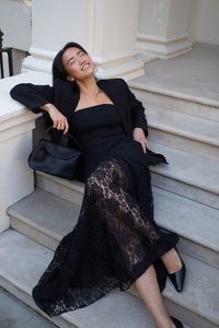 Juodas nėrinių maksi sijonas, dėvimas ant prigludusio juodo bešlepio suknelės, derinamas su juodu švarku ir atitinkančiu rankiniu krepšiu, ant akmeninių laiptų.