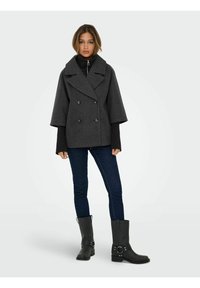 Dwurzędowy, szary płaszcz z wełny z dużym kołnierzem i rozszerzanymi rękawami, noszony na czarnej bluzce, w połączeniu z niebieskimi dżinsami i czarnymi kozakami za kolano.